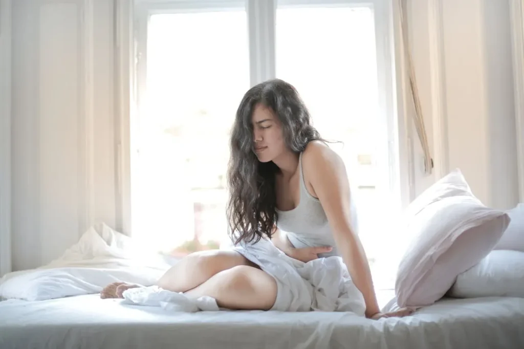 young lady placing her hands on her stomach in pains while sitting in a bed