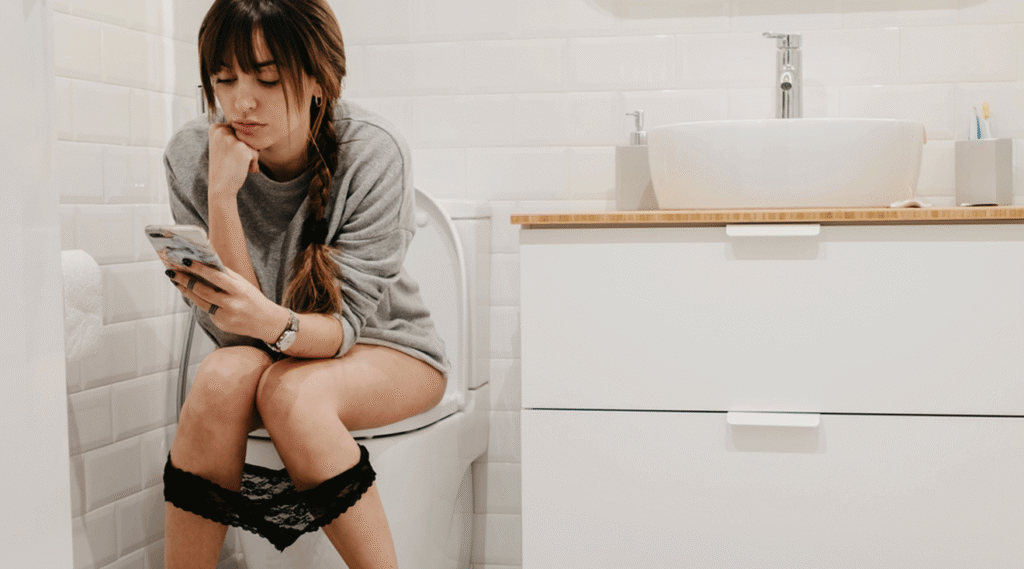 woman pressing her phone while using her toilet